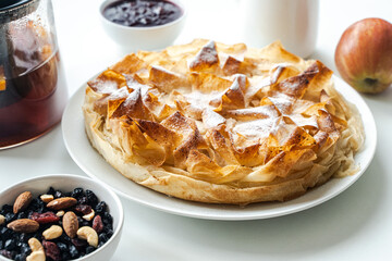 Homemade pastries, apple pie made of filet dough, nuts and tea on a white table. Selected focus. High quality photo