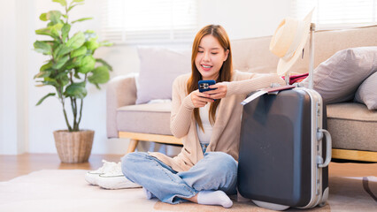 A young woman sitting next to her suitcase, using her smartphone to search for travel information, ready for her upcoming trip
