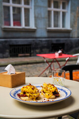 Delicious breakfast of poached eggs with bacon and potato pancakes with cheese sauce, street food.