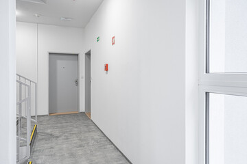 Bright, clean corridor with a minimalist design, featuring a gray floor, white walls, doors leading...