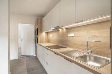 A modern, sleek kitchen with wooden countertops, white cabinets, and a stainless steel sink. The space is illuminated by under-cabinet LED strip lights, giving it a clean and contemporary feel.
