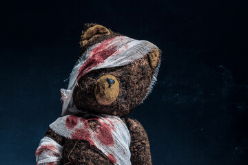 Old brown teddy bear wrapped in bloody bandages on a black background. Halloween concept
