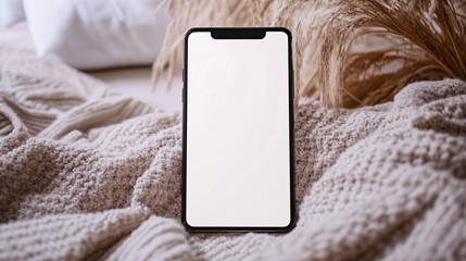 Modern smartphone with a blank white screen lies on a soft white knitted blanket.