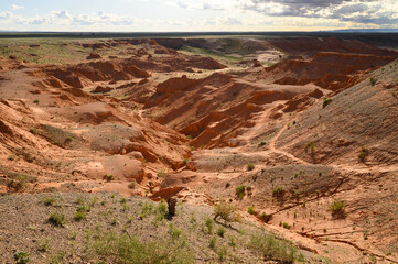 The Flaming Cliffs in the Gobi Desert, Mongolia, under a clear blue sky, showcasing its iconic red sandstone formations and barren landscape.
