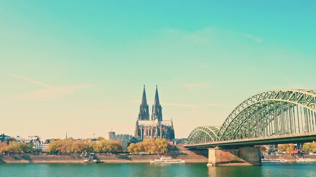 A bridge spans a river with a city in the background. The bridge is green and has a Gothic style