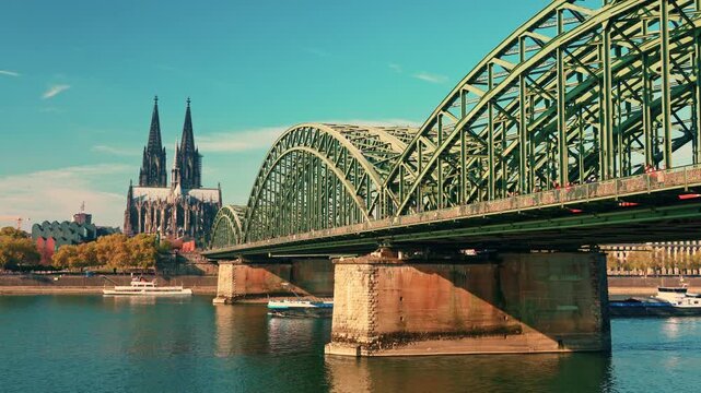 A bridge spans a river with a city in the background. The bridge is green and has a Gothic style