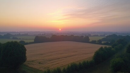 Beautiful sunset over a peaceful countryside, with the sky painted in soft pink and orange hues and fields below.