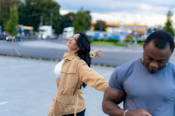 Fototapeta premium Woman joyfully dancing outdoors while a man prepares nearby. A woman dances with her arms outstretched while a man focuses on an activity nearby.