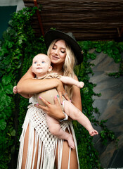 Mother holding baby in natural setting during sunny afternoon. A mother smiles while gently holding her baby amidst lush greenery.