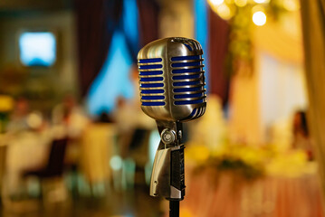 Vintage microphone on a stand in a dimly lit banquet hall. A retro microphone stands ready for a...