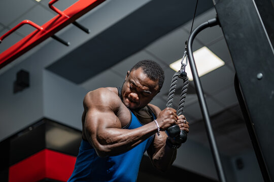 Man performing cable tricep pushdowns in a gym during daytime. A man focuses on his workout, executing cable tricep pushdowns in a gym.