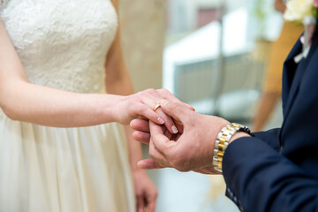 Couple exchanges wedding rings during ceremony in a bright venue. A groom places a wedding band on...