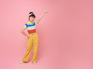 Smiling little asian girl looking and pointing finger shows place for your advertising text Isolated on pink copy space background.