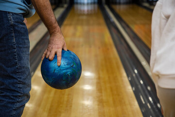 Obraz premium Man's hand holding blue bowling ball at bowling alley in club close-up