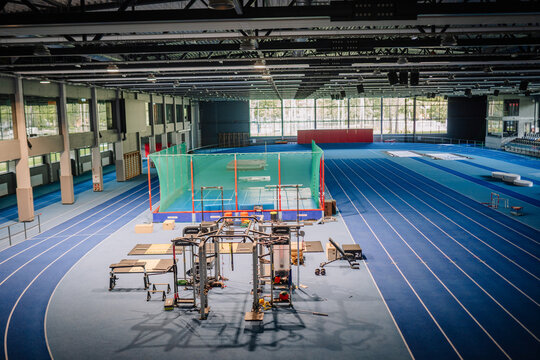 Valmiera, Latvia - August 17, 2024 -  Indoor athletics facility with blue tracks, exercise equipment, and a netted area for throwing sports, captured in bright natural light. Copy space...