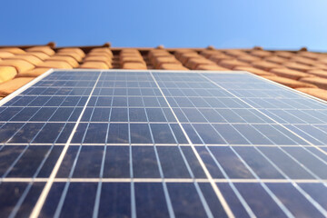 Highlight a solar panel on a house roof with a blue sky in the background. Emphasizing renewable and sustainable energy sources