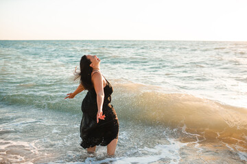 Happy beautiful overweight woman 30 - 35 year old wearing black dress walking at beach over sea close up. Body positive concept.