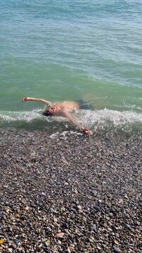 Man floating on back in ocean waves at the beach on vacation. Vertical video.