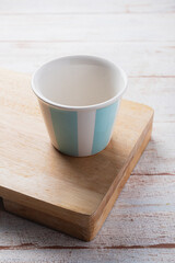 single empty ceramic tumbler cup. White inside and big turquoise stripes. over wooden board