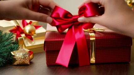 Holiday gift wrapped with gold ribbon placed beside decorated Christmas tree in cozy indoor setting