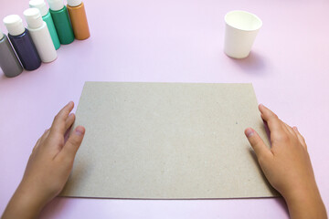 Obraz premium Paints, paper cup and sheet of paper holding hands on pink background. Acrylic painting.