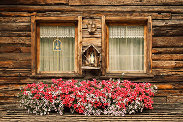 A cozy wooden cottage features vibrant flower boxes beneath its windows, radiating warmth and charm in Livigno, Italy.