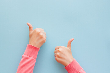 Two woman's hand in pink clothes is showing thumb up on blue background, motivation and success concept