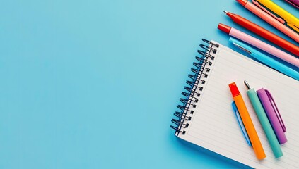 Blue background with spiral notebook and colorful pens.