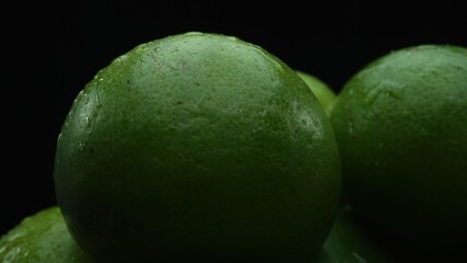 Slices of lime are meticulously arranged in a pile, set against a black background. Each lime slice is captured in stunning detail, its vibrant green hue and enticing texture. Close up. Comestible.