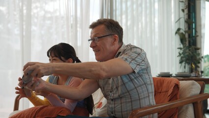 Fototapeta premium Grandfather and granddaughter together watch interesting entertainment media on TV. Old senior use technology communicate with young generation cross generation gap strengthen family bond. Divergence.