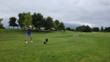 Golfer swinging a club on an overcast day at a lush green golf course