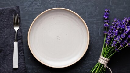 An empty grey plate (ceramic) on a dark grey background with a knife and fork, decorated with a bouquet of lavender and a napkin. A grey minimalistic concept with a place to copy text.