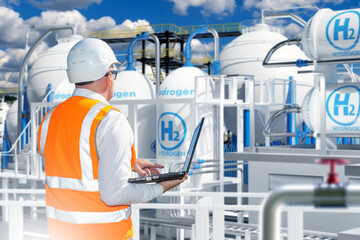 Hydrogen power plant technologist. Man on territory of energy enterprise. Guy with laptop near hydrogen tanks. Technologist inspects factory with his back to camera. Hydrogen technologies