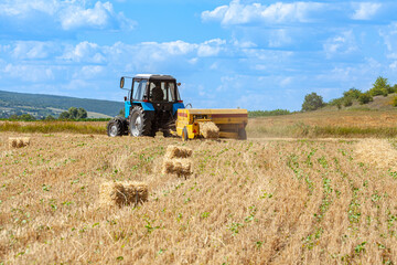 Obraz premium Close-up of hay baling with a tractor using a baler on a cloudy summer day, a large bale comes out of the baler. 