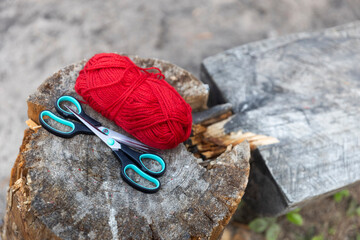 Red woolen yarn and two pairs of scissors lying on a tree stump near a tent in a campsite in a pine...
