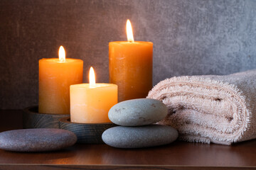 Spa still life with candles, towels and pebbles on wooden background.