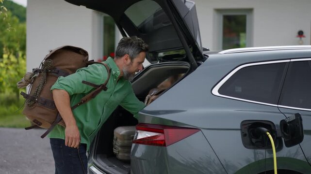 Father with son loading luggage into trunk of electric car with charger in charging port. Travelling on family road trip or vacation by electric vehicle.