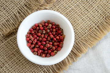 Red or pink peppercorns on wooden spoon on grey textured linen background