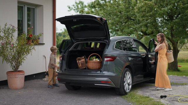 Father charging electric car after grocery shopping in supermarket. Plugging charger into electric vehicle in front of house.