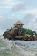 Vertical photo of a cabin on a hill surrounded by rocks and vegetation in Tayrona Park in Santa...