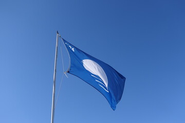 Zoom photo of 2024 blue flag representing cleanliness of the seas certifying marine quality standards waving in deep blue sky