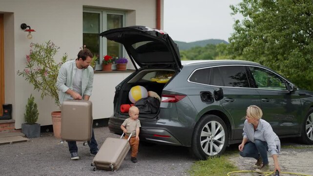 Family loading luggage into trunk of electric car with charger in charging port. Travelling on family road trip or vacation by electric vehicle.