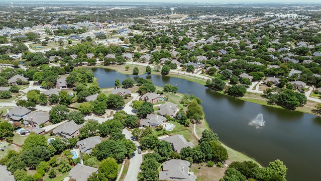 Master planned community with neighborhood pond water fountain, mature trees surrounding row of upscale two-story houses, swimming pool, in Keller, Tarrant County, Texas, suburbs Dallas, aerial