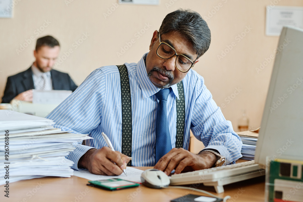 Aufkleber manager reviewing documents at office desk, concentrating with a focused expression. piles of papers