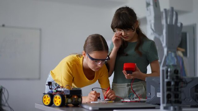 Two girl classmates working togeter on circuit board, building robotic car in after-school robotics club. Children learning robotics in Elementary school.
