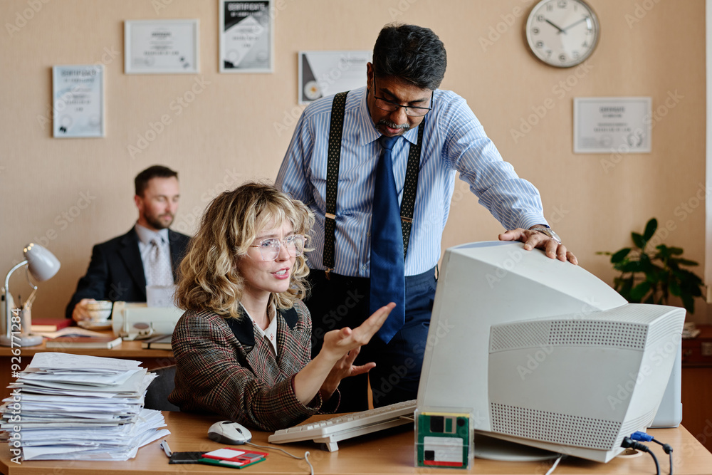 Aufkleber Two coworkers engaging in discussion over computer monitor in office setting with certificates on wall. Woman pointing at screen while man observes attentively