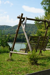 A rustic wooden swing in a beautiful Austrian meadow, with green grass, a clear sky, surrounding...