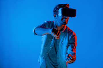 Smart man wear virtual goggle while move driving car hand gesture. Caucasian teenager using futuristic digital technology to enter virtual world while standing at colorful neon background. Deviation.