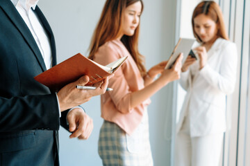 Fototapeta premium Happy young handsome businessman reading book and working in office with colleagues and friend at workplace. Corporate business people group. uds