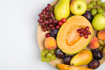 A plate filled with a variety of fruits, melon, apple, pear, grapes and peach on a light background. Top view, horizontal, free copy space.